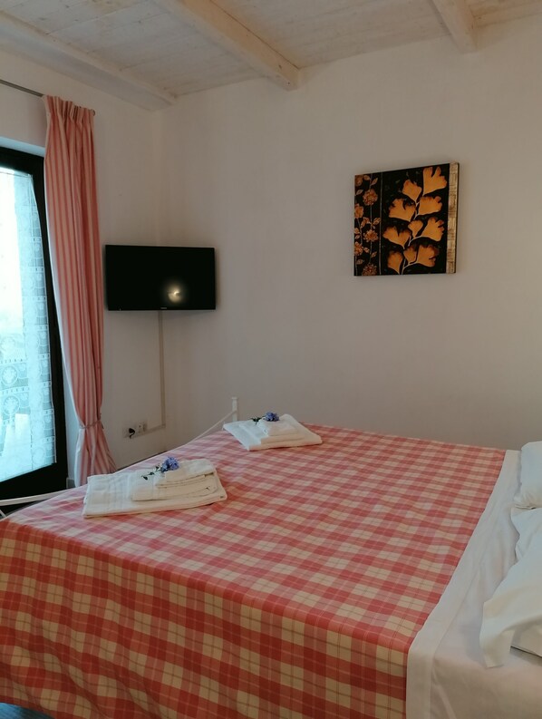 A hotel room with a checkered bedspread, a flat-screen TV mounted on the wall, and a painting above the bed.