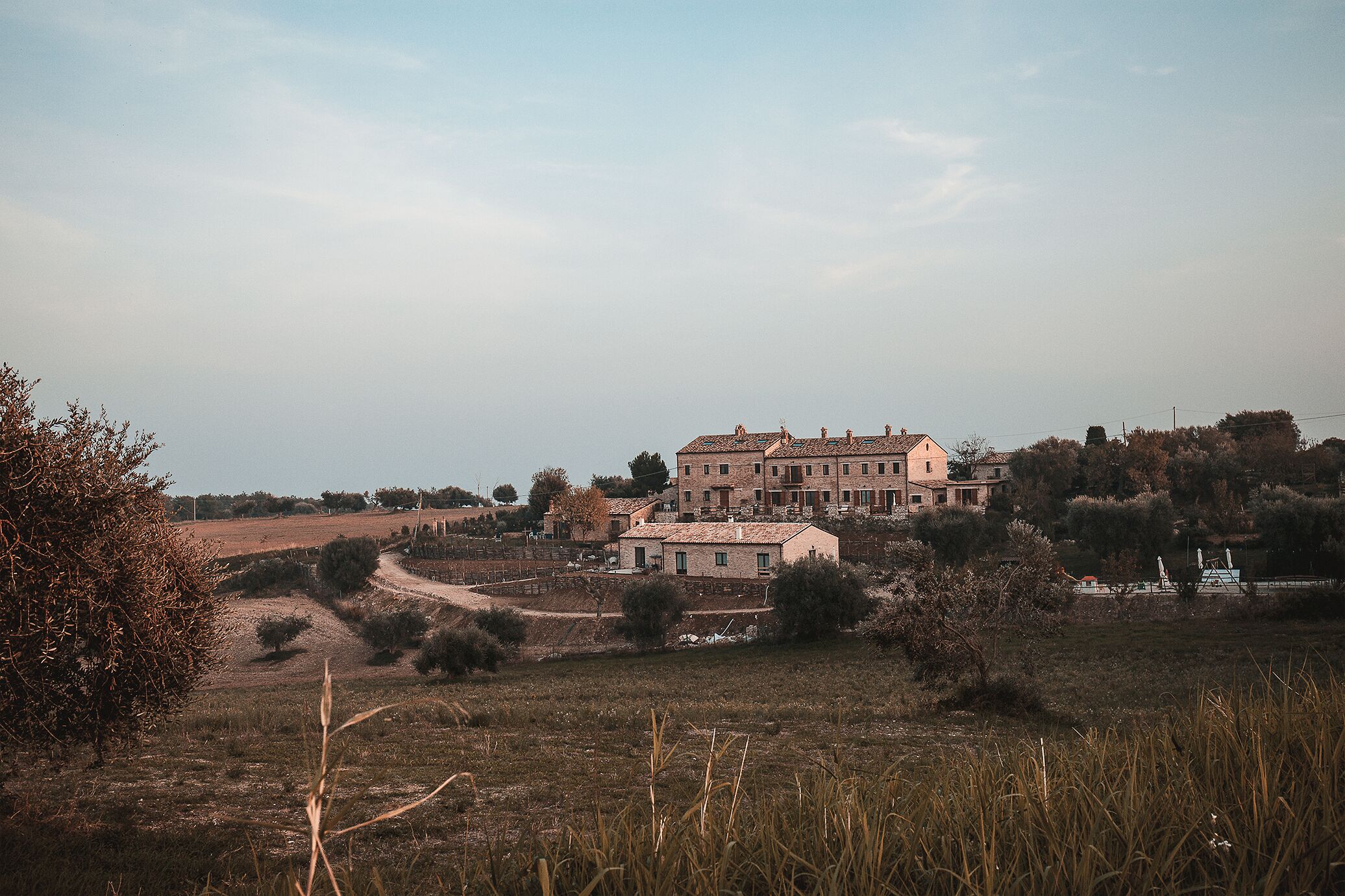 A large, multi-story building with a traditional architectural style, surrounded by open fields and sparse vegetation.