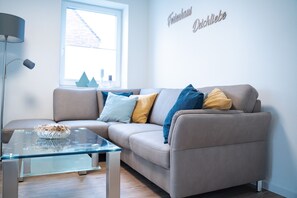 A modern living room with a grey sofa, a glass coffee table, and a lamp.