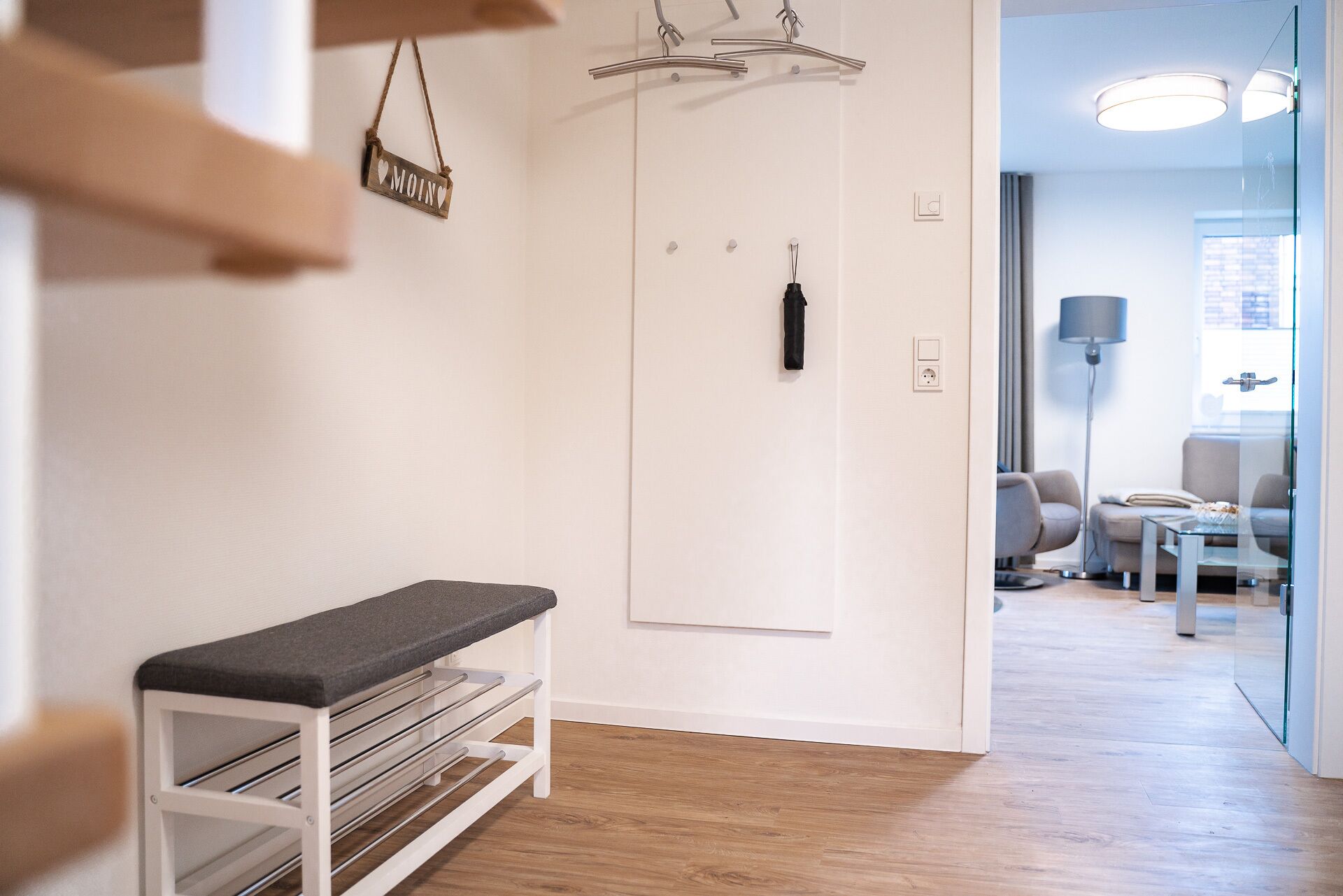 A modern hotel room with a bench, a coat rack, and a door with a black handle.