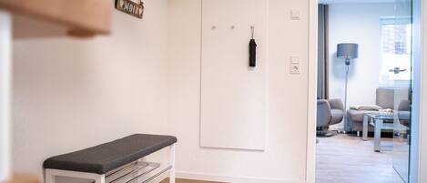 A modern hotel room with a bench, a coat rack, and a door with a black handle.