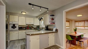 Een moderne keuken met witte kastjes, een granieten aanrecht en een eethoek met een houten tafel en groene stoelen.