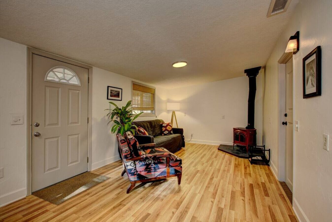 Ein Wohnzimmer mit Holzboden, einer Couch, einem gemusterten Sessel, einer Pflanze, einem Kamin und einer Tür mit Fenster.