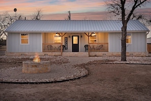 A small building with a metal roof, a front door, and a fire pit in the foreground. - Cherry Mountain, Hot tub, Fire pit, Views! (Fredericksburg)