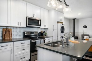 A modern kitchen with white cabinets, stainless steel appliances, and a central island with a sink. - Cherry Mountain, Hot tub, Fire pit, Views! (Fredericksburg)