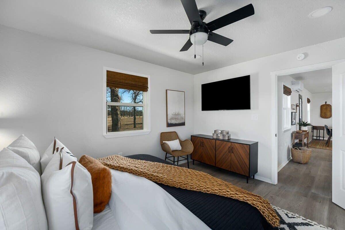 A modern bedroom with a bed, a desk, a chair, a ceiling fan, and a TV.