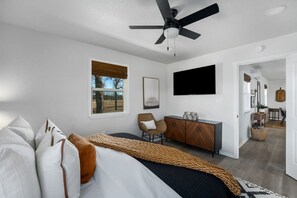 Ein modernes Schlafzimmer mit einem Bett, einem Schreibtisch, einem Stuhl, einem Deckenventilator und einem Fernseher.