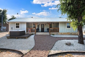 A single-story building with a metal roof, a front porch with wooden railings, and a hot tub in the front yard. - Cherry Mountain, Hot tub, Fire pit, Views! (Fredericksburg)