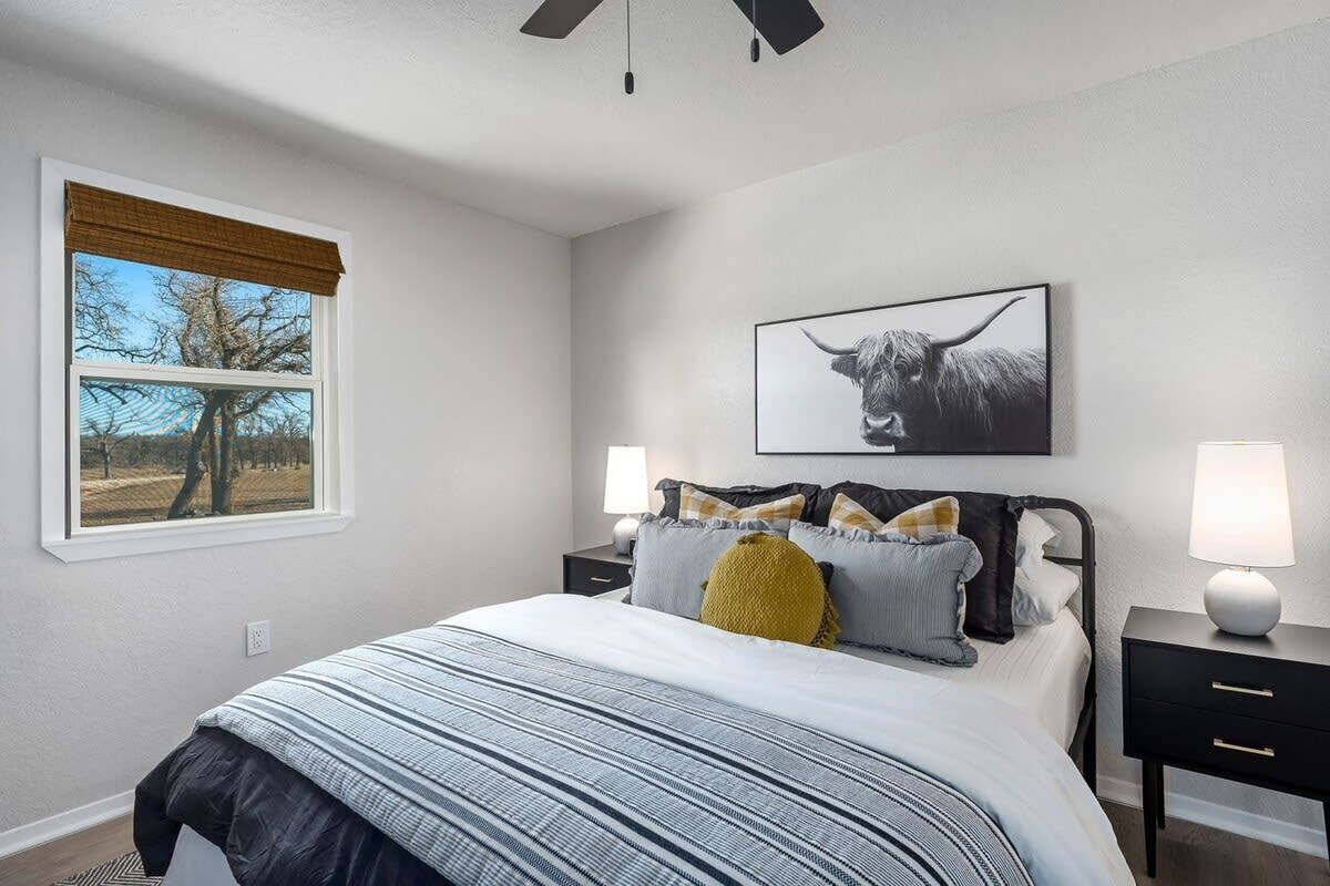 Ein Schlafzimmer mit einem Bett, zwei Nachttischen, einem Fenster mit Aussicht und einem an der Wand hängenden Bild.