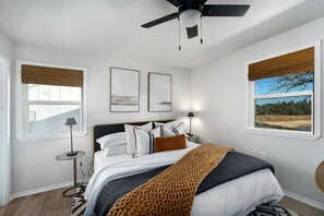 Ein Schlafzimmer mit einem Bett, zwei Nachttischen, einem Deckenventilator und zwei Fenstern mit Jalousien.