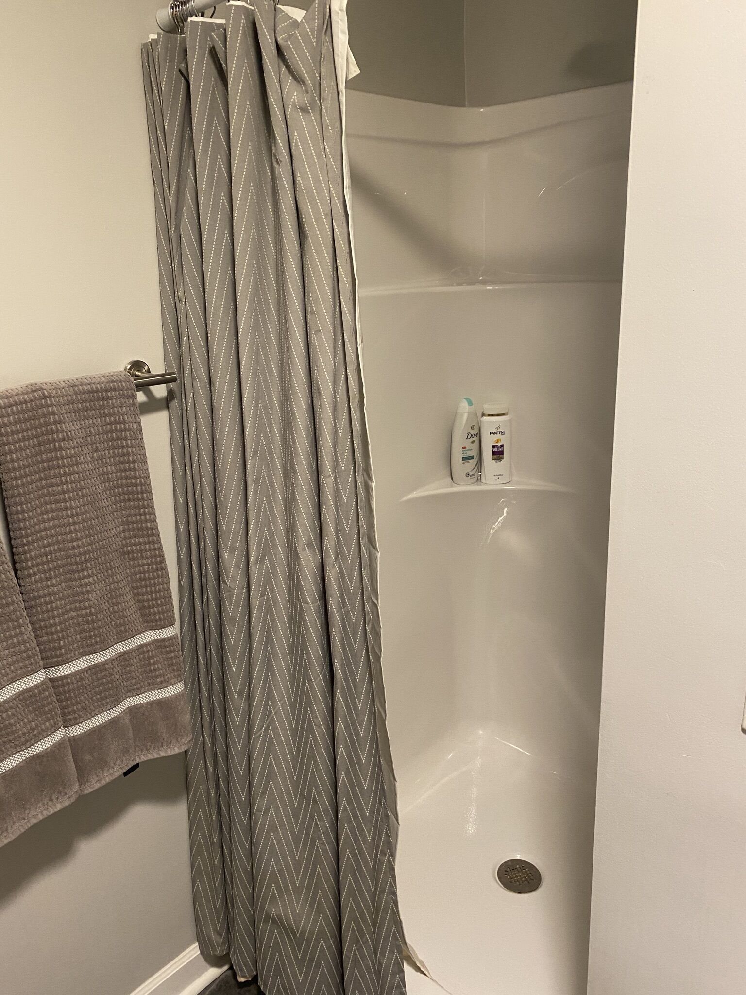 A shower area with a grey chevron-patterned shower curtain, a towel rack with a brown towel, and a shelf with toiletries.