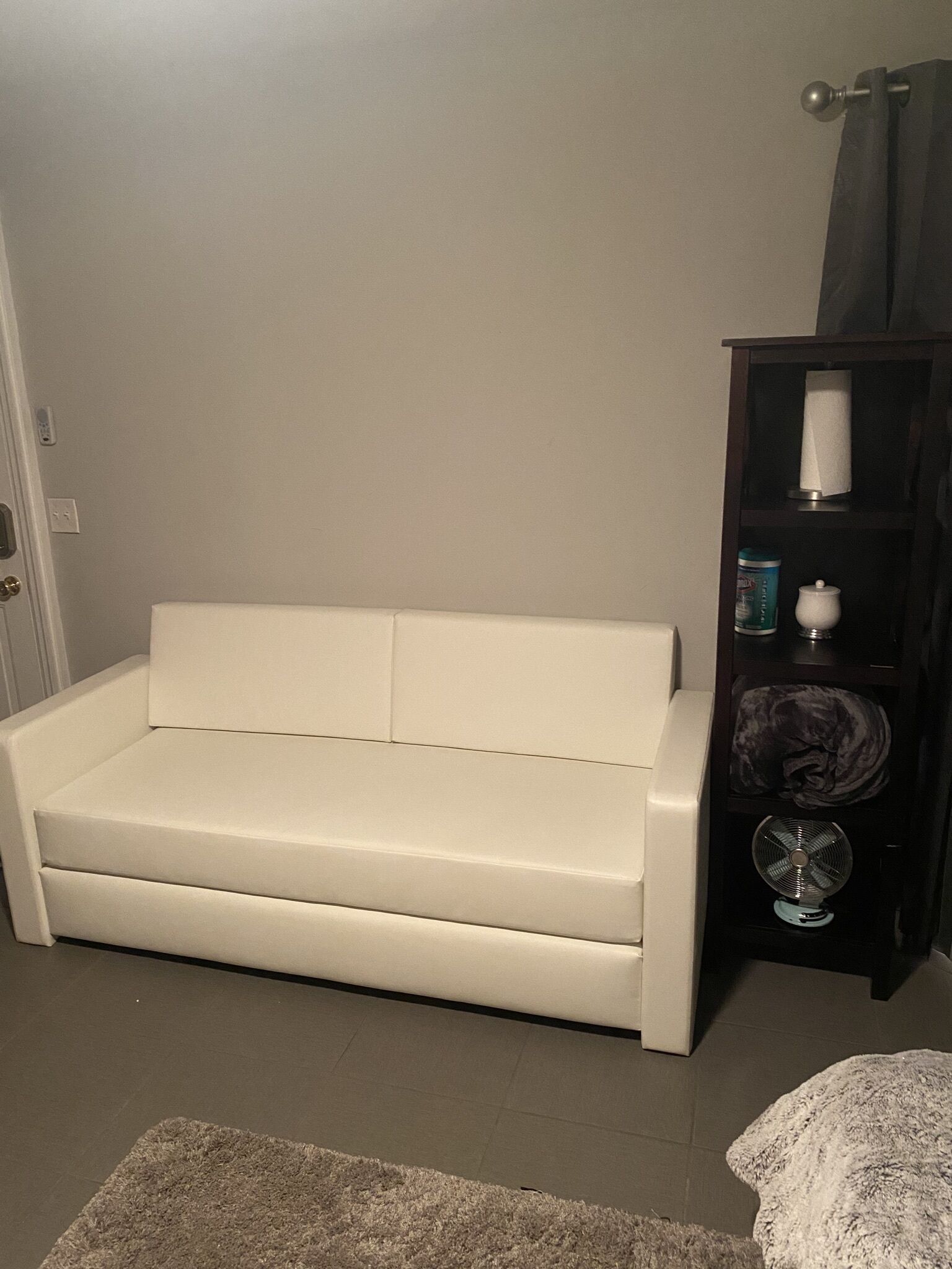 Un sofá blanco en una habitación con un mueble de madera oscura que contiene un ventilador, un roll de pañuelos y una lata.