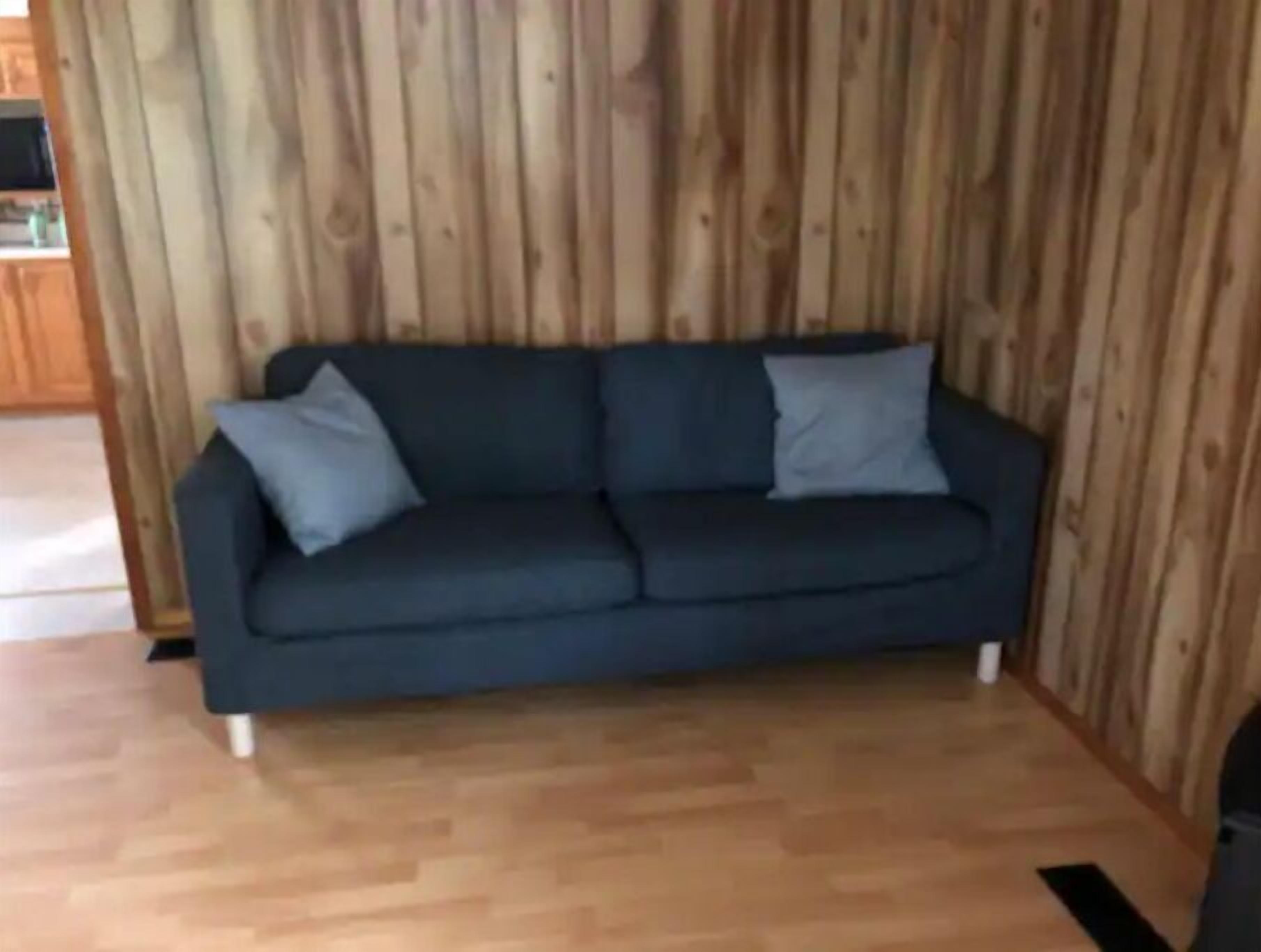 Un sofá oscuro con dos almohadas frente a una pared de madera.