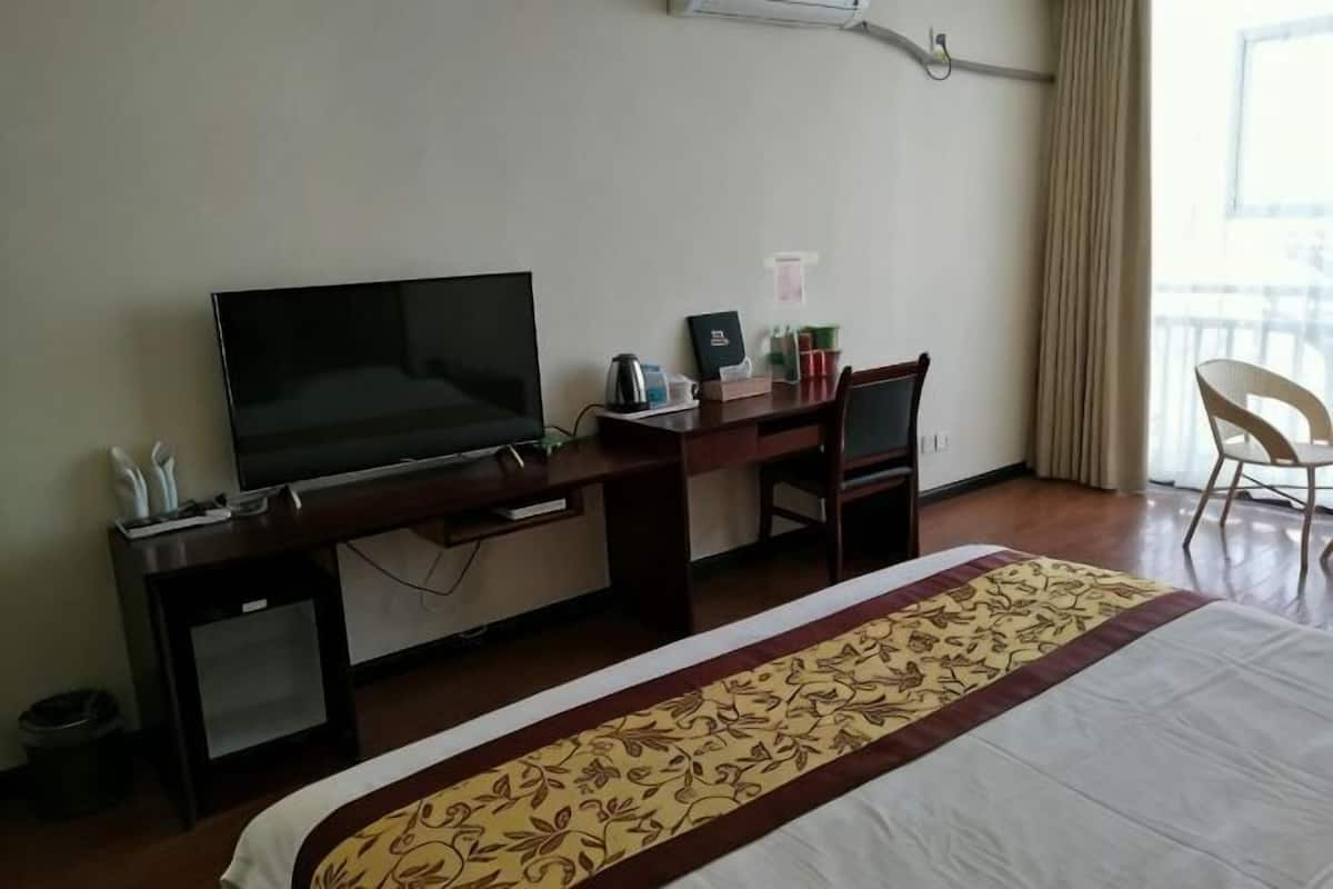 Habitación de hotel con cama, escritorio con televisor, silla y ventana con cortinas.