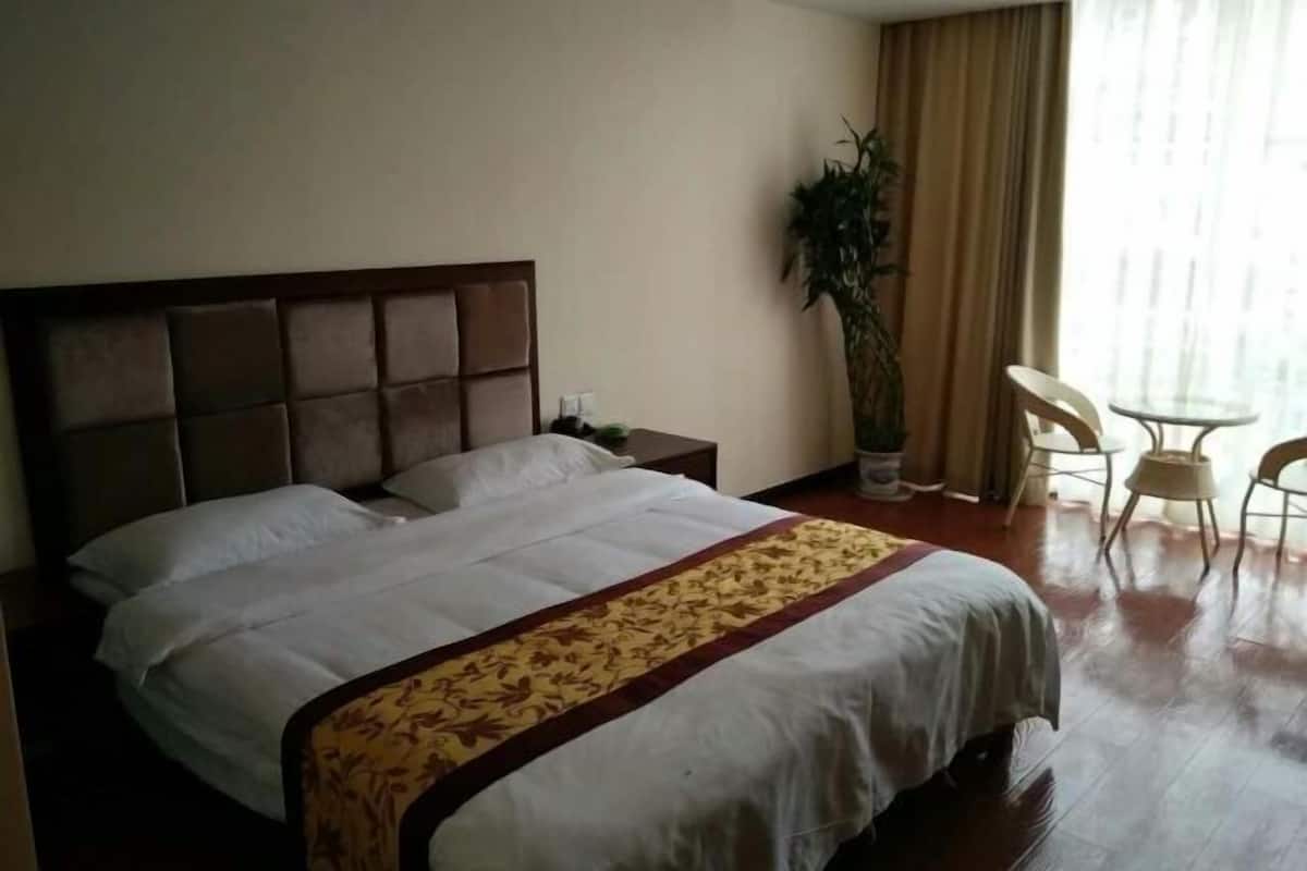 Una habitación de hotel con una cama, una mesita de noche, una planta en maceta y una pequeña mesa con sillas.