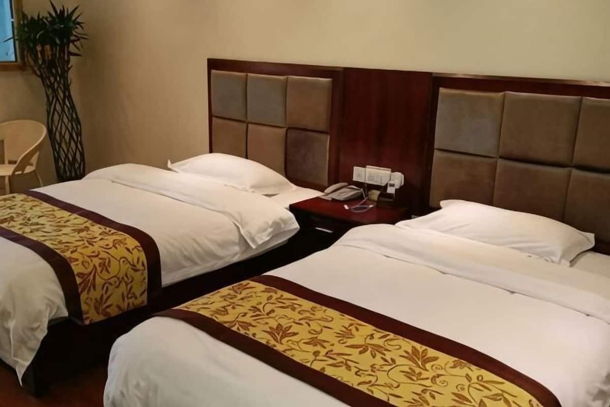 Dos camas individuales con cabeceras, una mesita de noche con teléfono y una silla en una habitación de hotel.