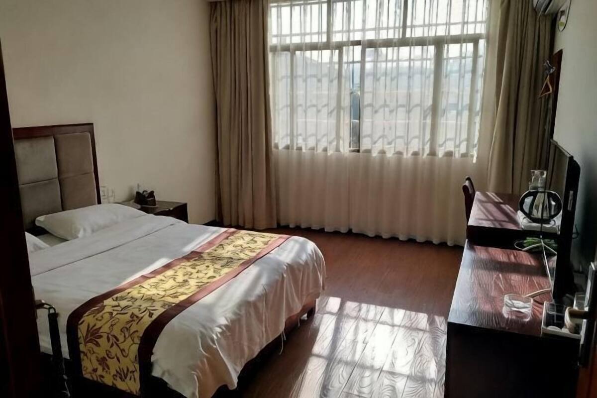 Habitación de hotel con cama, escritorio, silla, ventana con cortinas y vista a un edificio.