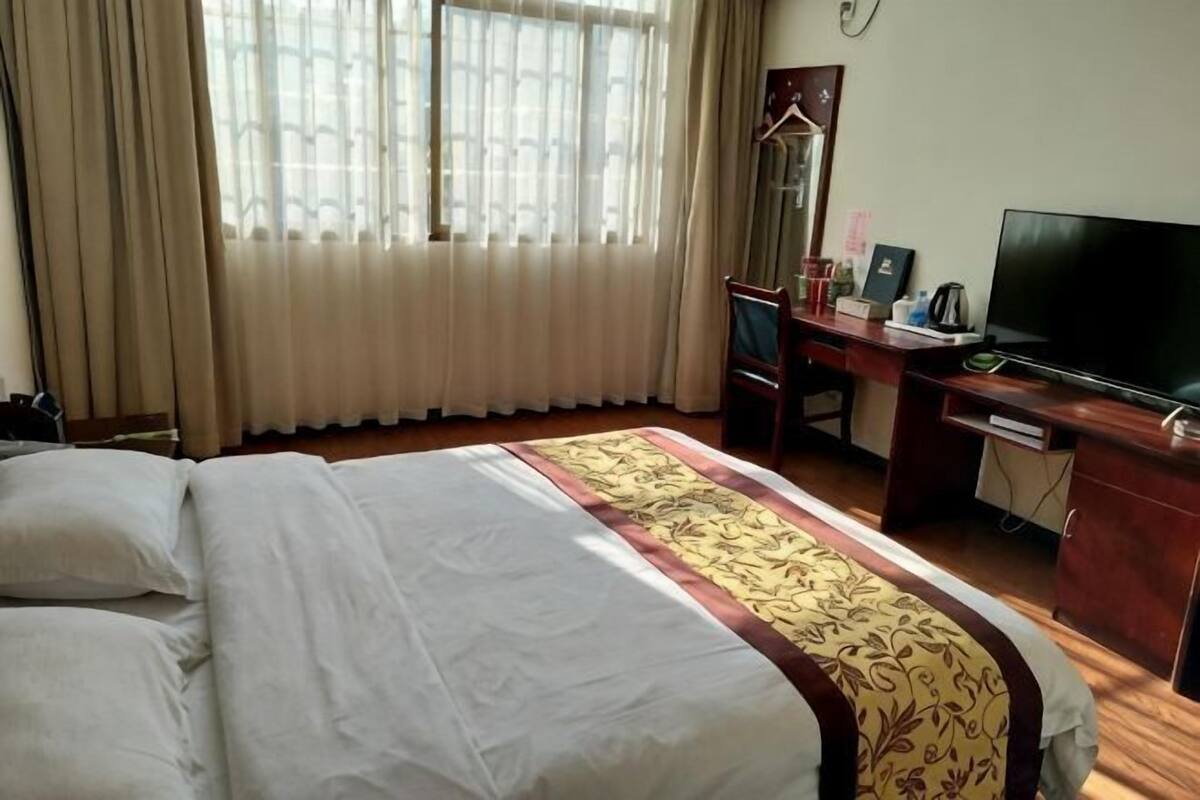 Una habitación de hotel con cama, escritorio, televisor y ventana con cortinas.
