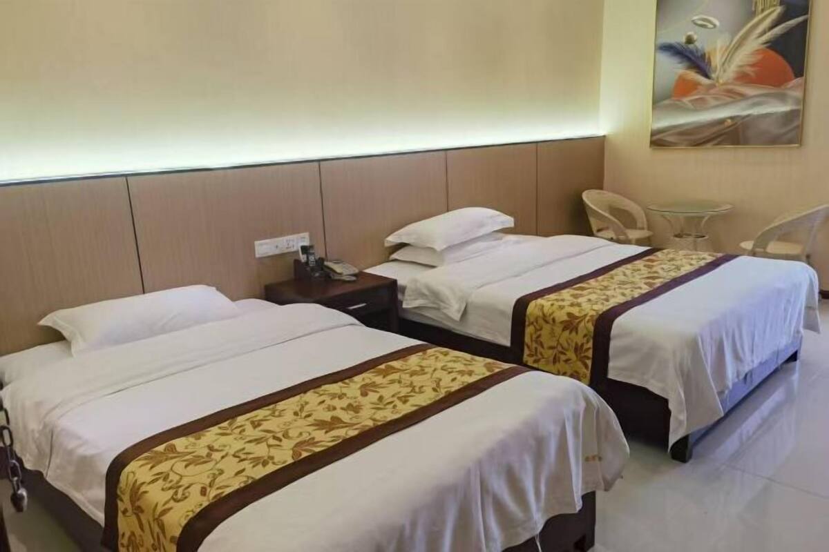 Una habitación de hotel con dos camas, una mesita pequeña, una silla y un cuadro en la pared.