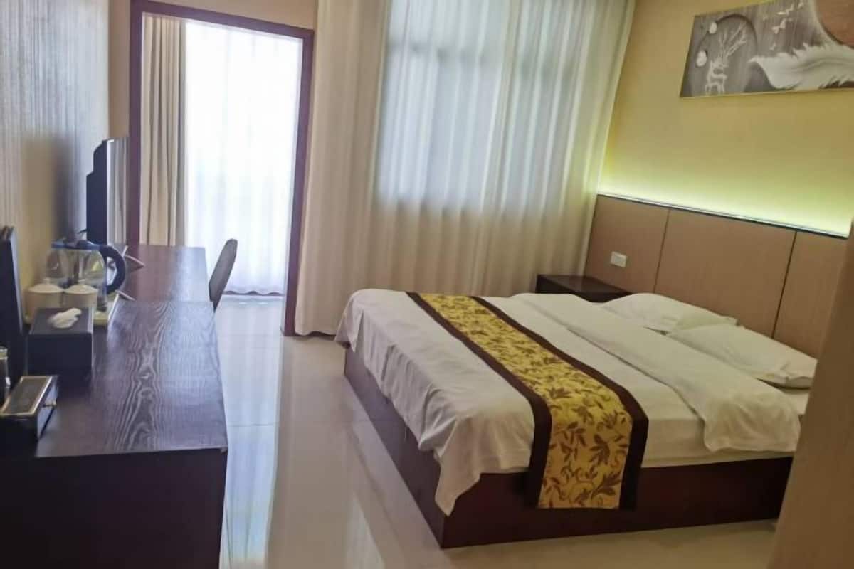 Una habitación de hotel con cama, escritorio, televisión y ventana con cortinas.