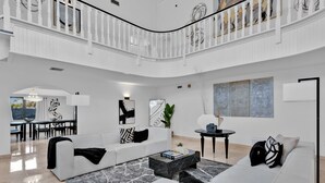 A spacious living area with a high ceiling, white walls, and a curved staircase. - Villa Maya: 12 BR, 14k sq. ft. estate with pool, pickle ball, bball, disco club! (Miami)