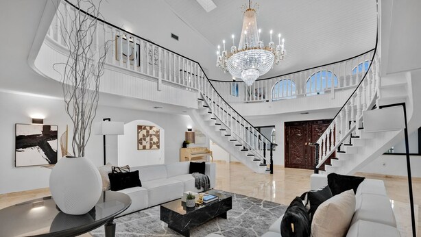 A spacious living area with a grand staircase, a chandelier, and a high ceiling. - Villa Maya: 12 BR, 14k sq. ft. estate with pool, pickle ball, bball, disco club! (Miami)
