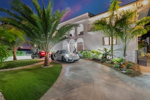 Une maison moderne avec une allée, des palmiers et une voiture décapotable garée devant.