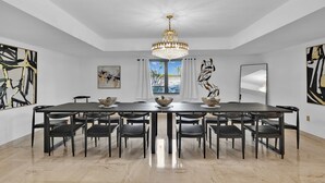 A spacious dining area with a long table, multiple chairs, a chandelier, and abstract art on the walls. - Villa Maya: 12 BR, 14k sq. ft. estate with pool, pickle ball, bball, disco club! (Miami)