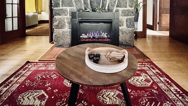 A living room with a stone fireplace, a mounted television, and a red patterned rug.