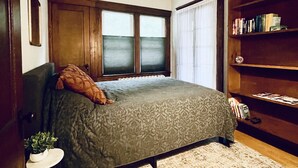 A bedroom with a bed, a bookshelf, a window, and a small table with a plant.