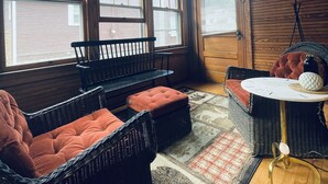 A cozy room with wooden walls and ceiling, featuring a bench, wicker furniture, a small table, and a lamp.