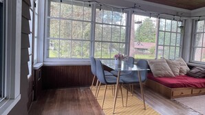 A room with a wooden ceiling, large windows, a bed, a table with chairs, and a rug.