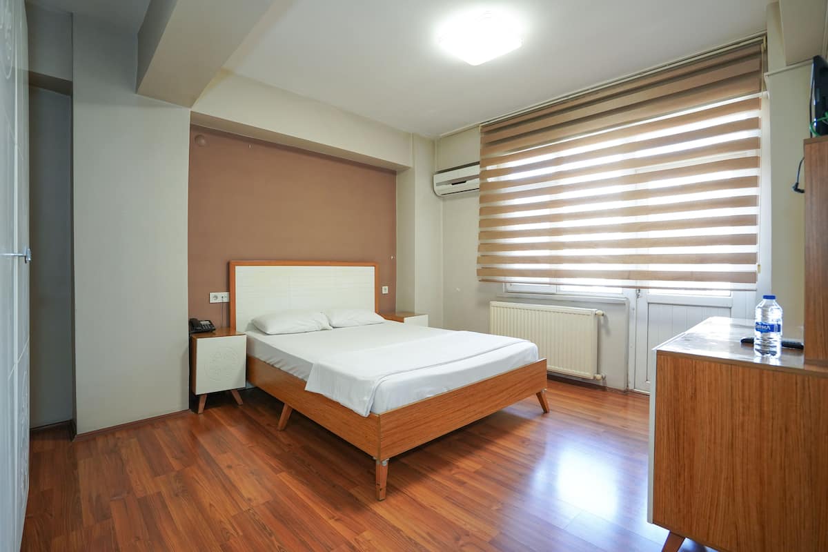 Un dormitorio con cama de madera, mesita de noche, radiador y ventana con persianas.