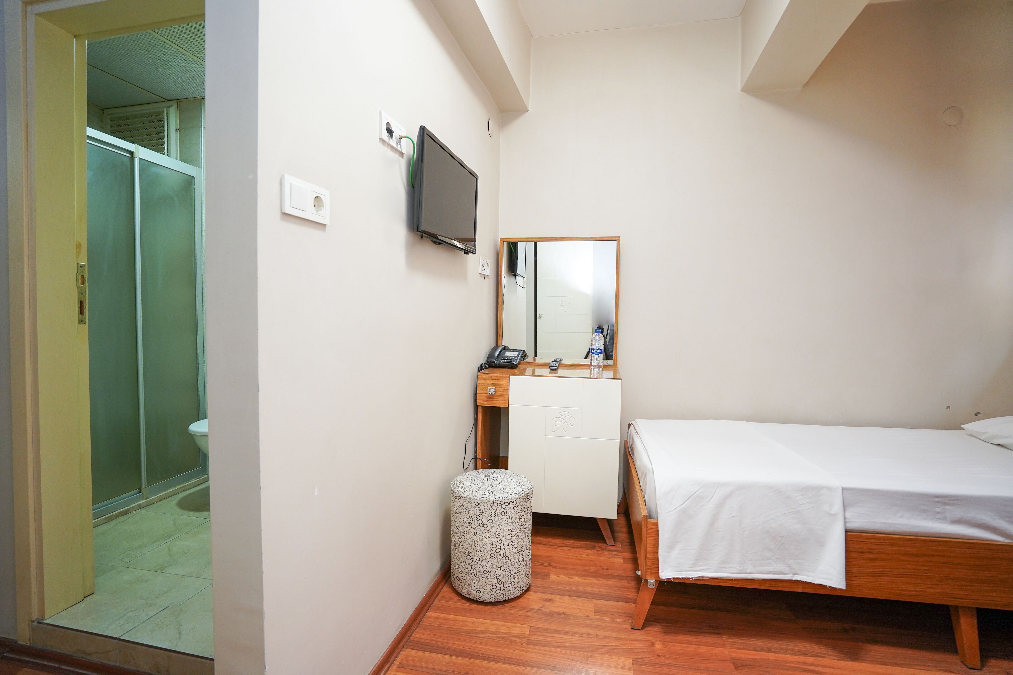 A small, clean room with a bed, a mirror, a TV, and a toilet.