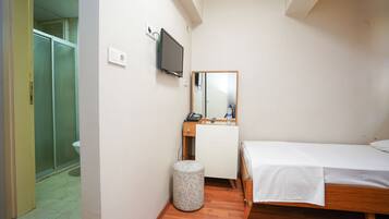 A small, clean room with a bed, a mirror, a TV, and a toilet.