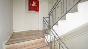 A staircase with a metal railing, wooden steps, and a red fire safety box on the wall. - İpek Otel (Balikesir)