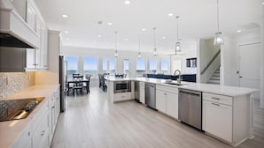 A modern kitchen with white cabinetry, stainless steel appliances, and pendant lighting. - The Beach Club 8BR OF House in Cherry Grove (North Myrtle Beach)