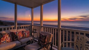 Un balcón con un sofá y sillones, con vistas a la puesta de sol sobre el océano.