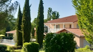 A two-story house with a red-tiled roof, surrounded by lush greenery and tall cypress trees. - Beautiful architect-designed villa with swimming pool in the middle of a large park 10 minutes from Auch. (Auterive)