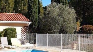 A swimming pool with a white fence, surrounded by tall trees and a building with a tiled roof. - Beautiful architect-designed villa with swimming pool in the middle of a large park 10 minutes from Auch. (Auterive)