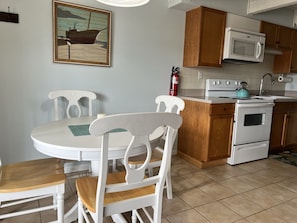 A kitchen with white cabinets, a white stove, a white microwave, and a wooden table with white chairs.