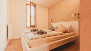 Una cama individual con estructura de madera, una ventana con persianas y una lámpara fijada a la pared.