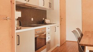 Una cocina funcional con armarios blancos, una estufa y una zona de comedor con una mesa y sillas de madera.
