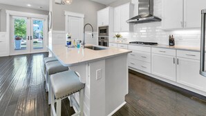 Een moderne keuken met witte kasten, een roestvrijstalen afzuigkap en een centraal keukenblok met barstoelen.