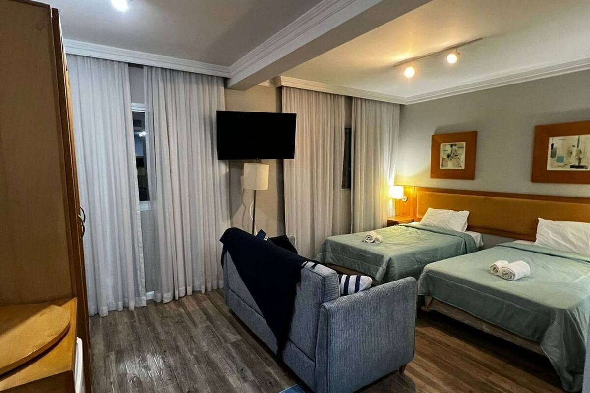 Ein Hotelzimmer mit zwei Einzelbetten, einer Couch, einem Fernseher und Holzboden.