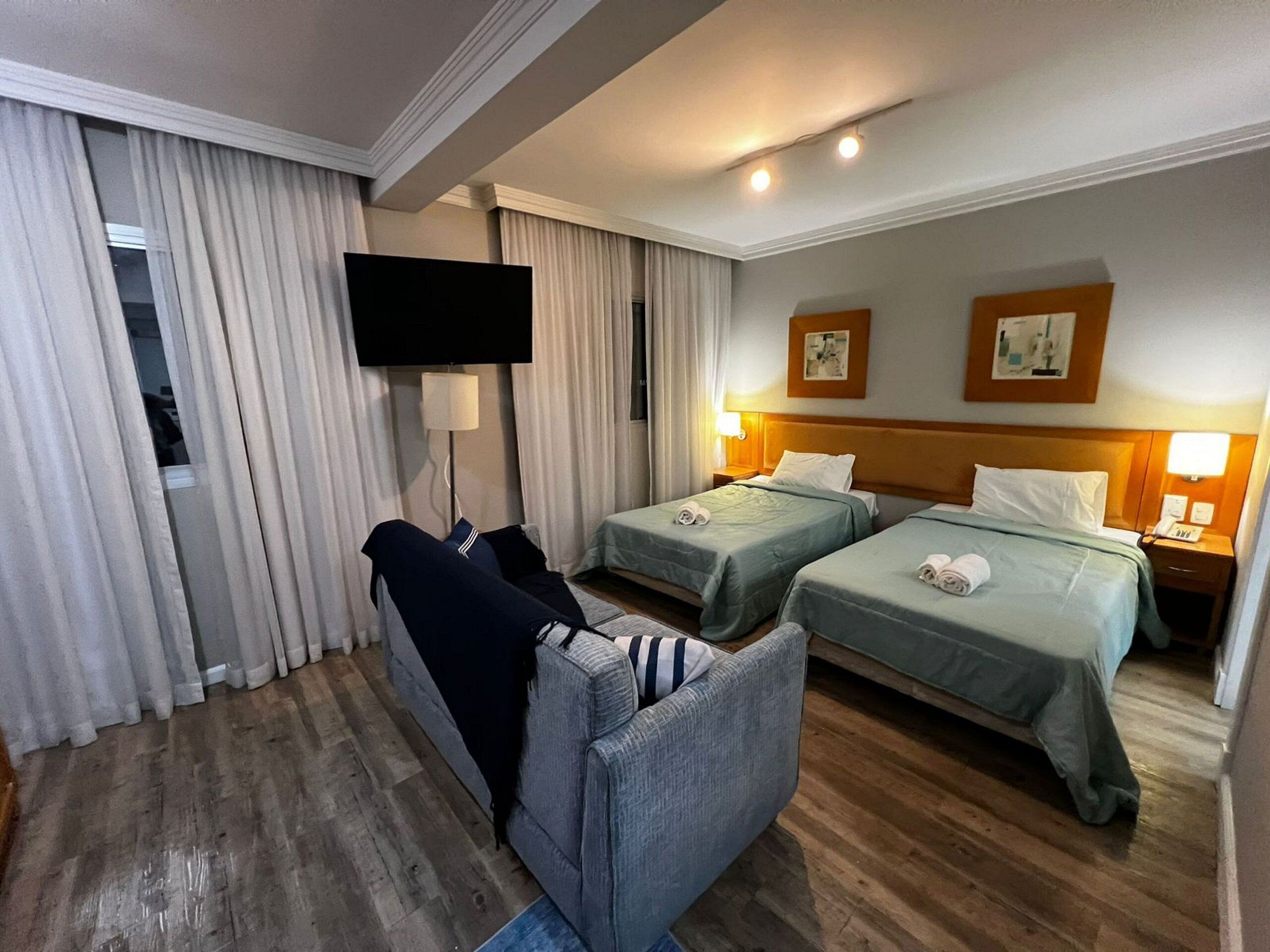 Habitación de hotel con dos camas, un sofá, un televisor y un televisor de pantalla plana montado en la pared.