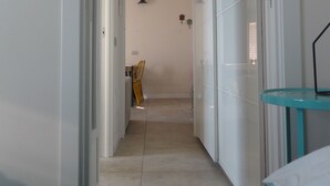 A narrow hallway leading to a bedroom with a bed, a small table, and a wardrobe.