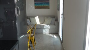 A modern kitchen with a black refrigerator, a dining area with a yellow chair, and a living room with a sofa and a painting.