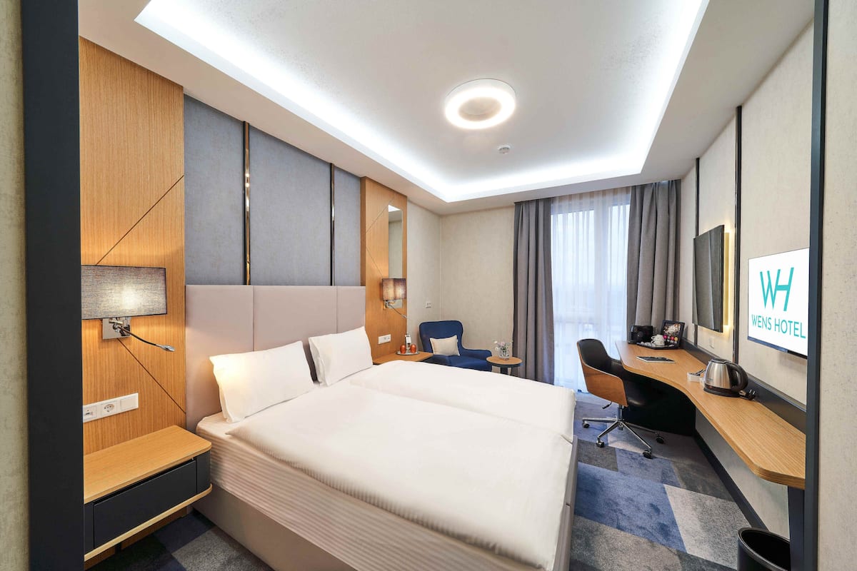 Ein Hotelzimmer mit einem großen Bett, einem Schreibtisch, einem Sessel, einem Fernseher und einem Fenster mit Vorhängen.