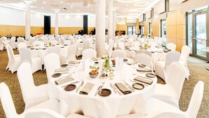 A large banquet hall with round tables set for dining, white chairs, and a modern ceiling design. - WENS Hotel (Mainz)